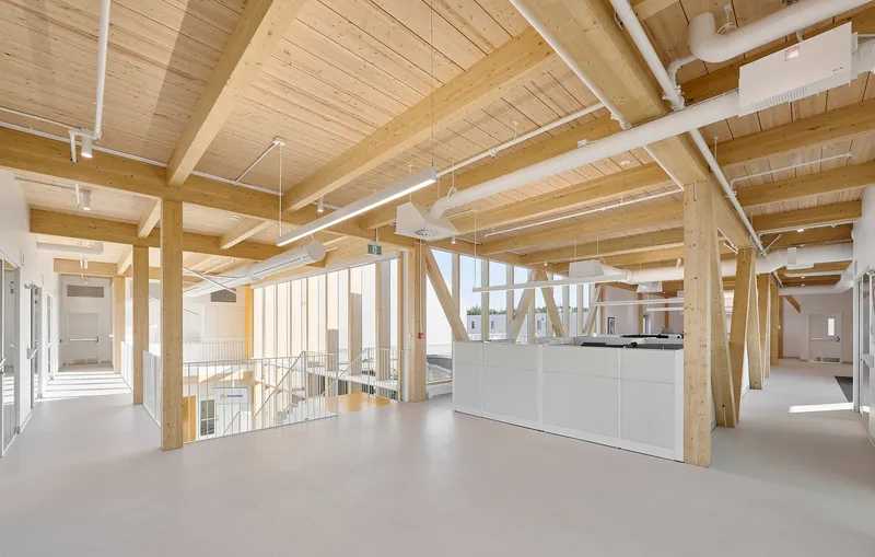 Upper-level open workspace with exposed timber beams and a white central millwork unit overlooking the floor below