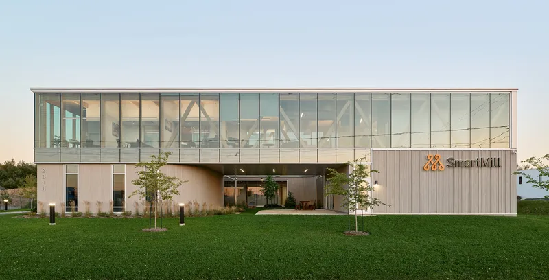 Front elevation showing glass upper volume and recessed entry flanked by young trees at dusk