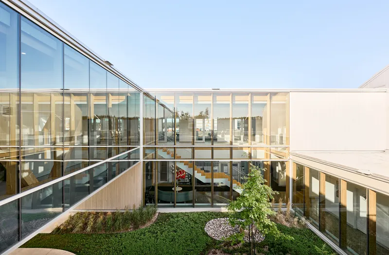Interior courtyard with planted beds and sloped glass wall revealing office spaces beyond