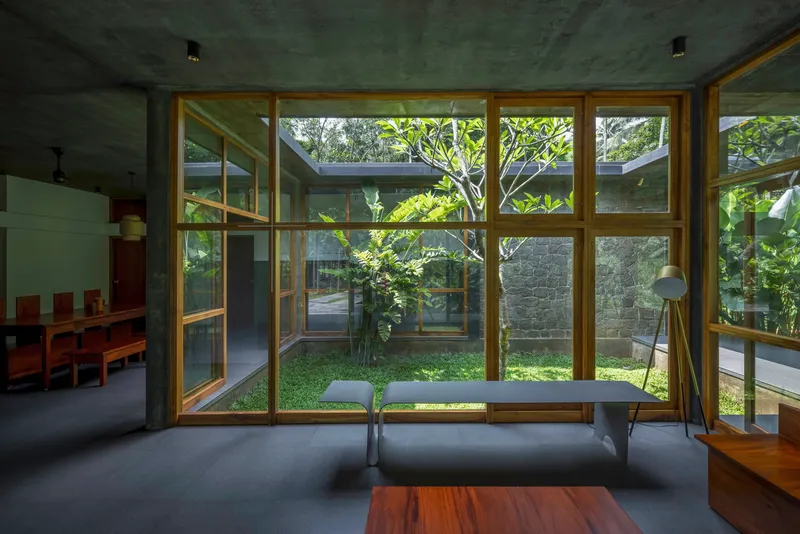 Interior view through timber window wall to courtyard with tree and stone wall beyond