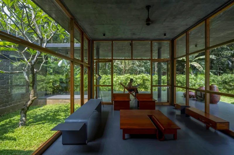 Living room with floor-to-ceiling timber-framed glazing opening onto a lawn with two seated figures beyond