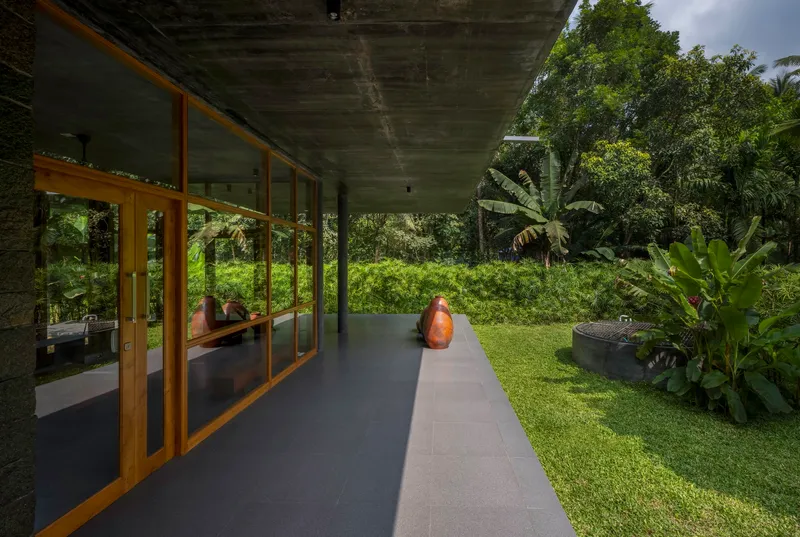 Concrete overhang sheltering a walkway with timber framed glazing overlooking a lawn and banana plants