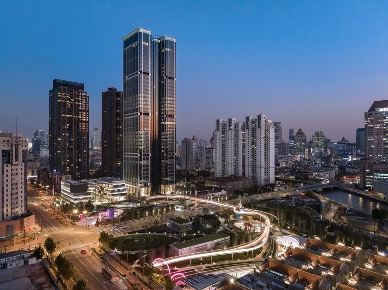Aerial view of twin glass towers rising above a spiraling pedestrian bridge at dusk