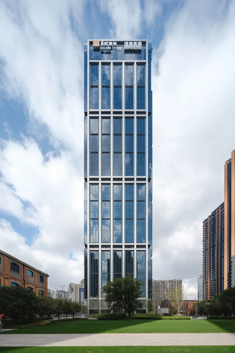 Single tower with vertical glass and white panel facade rising above a green lawn under cloudy skies
