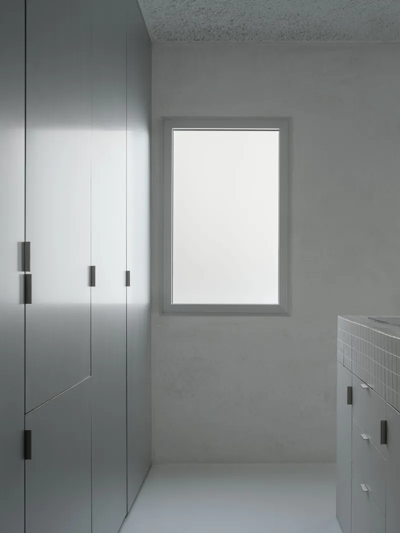Corridor with brushed steel wardrobes, white-framed window and mosaic tile vanity counter at end