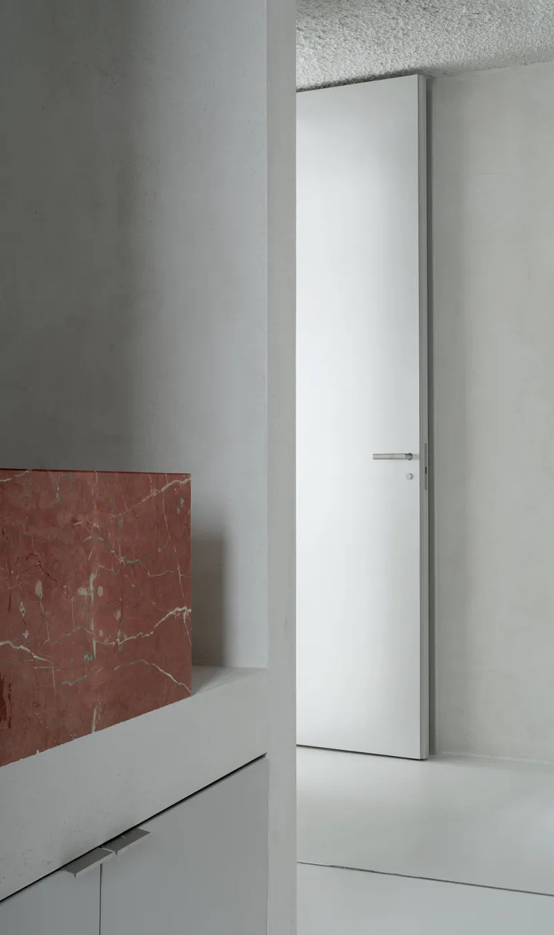 White flush door set into plaster walls with red marble wainscoting and terrazzo ceiling panel