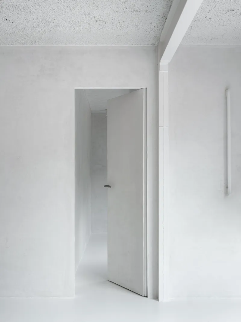 Open doorway framing a white corridor with terrazzo ceiling and continuous plaster walls