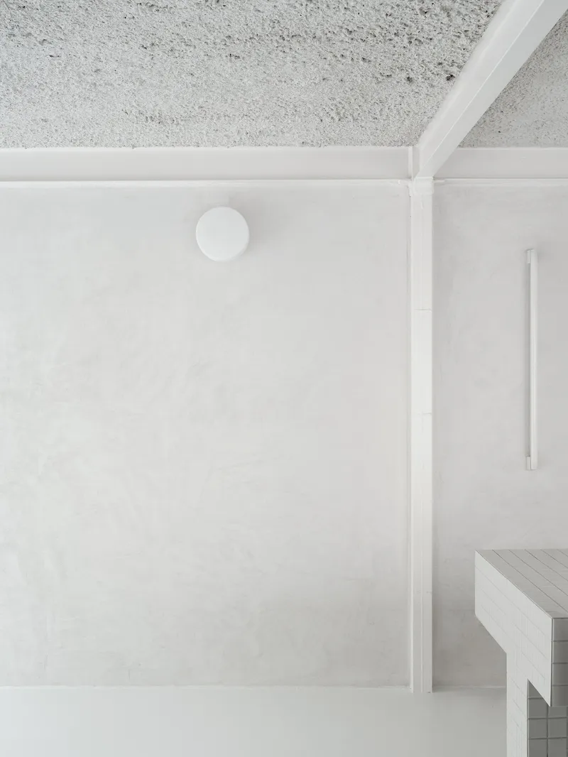Top-down view of a white plaster ceiling with exposed concrete above and partial timber bench below