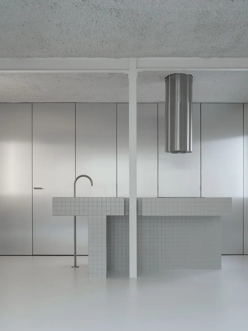 Kitchen island with white mosaic tile and stainless steel faucet beneath a cylindrical range hood