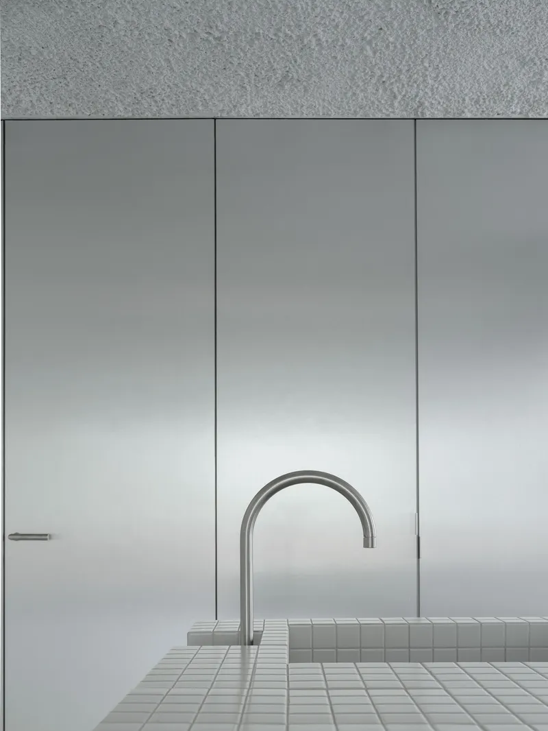 Close-up of a curved stainless steel faucet rising from a white mosaic tiled counter