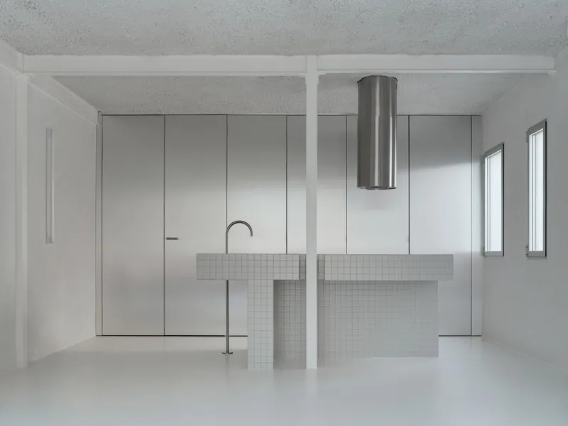 Open kitchen with white mosaic tile island, cylindrical steel range hood and brushed steel cabinet wall
