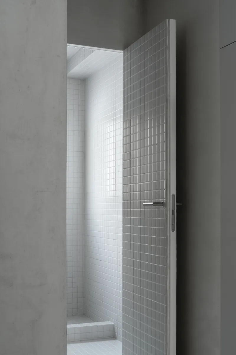 Narrow doorway opening to white mosaic tiled room lit by natural daylight from above
