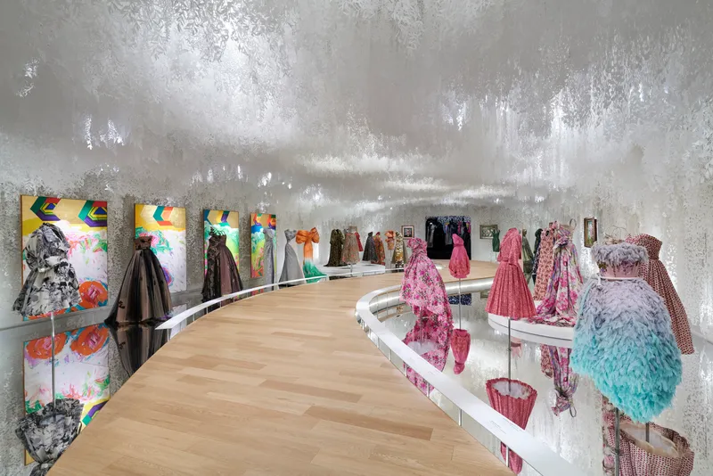 Curved exhibition platform with light wood flooring against silver foil-clad walls and colorful graphic panels