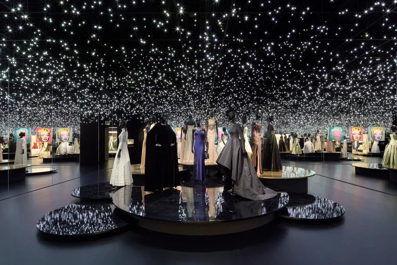 Black gallery space with circular platforms beneath a ceiling covered in thousands of small lights