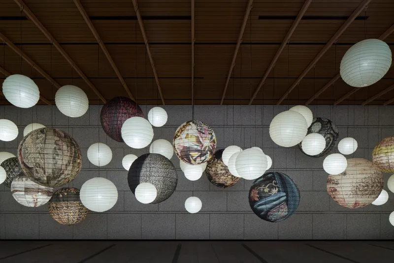 Gallery ceiling with patterned paper lanterns of varying sizes suspended above a tiled wall