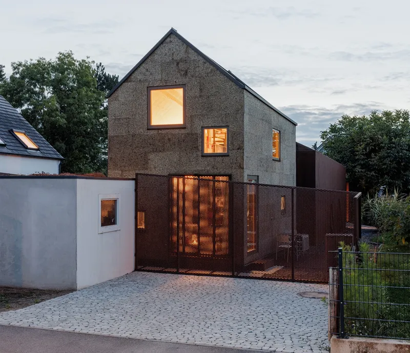 Street facade at dusk with glowing windows and illuminated interior visible through perforated copper gate