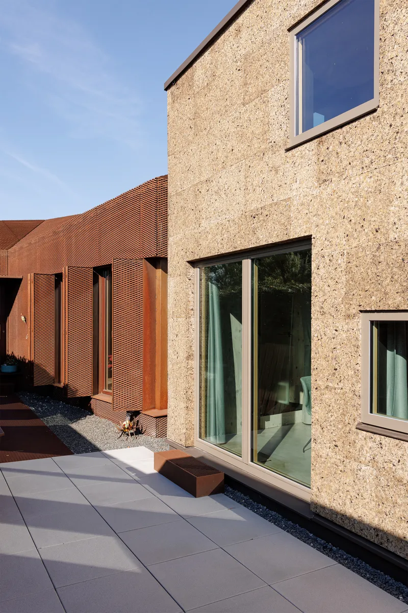 Courtyard terrace with grey pavers meeting cork facade and curved perforated copper screen wall