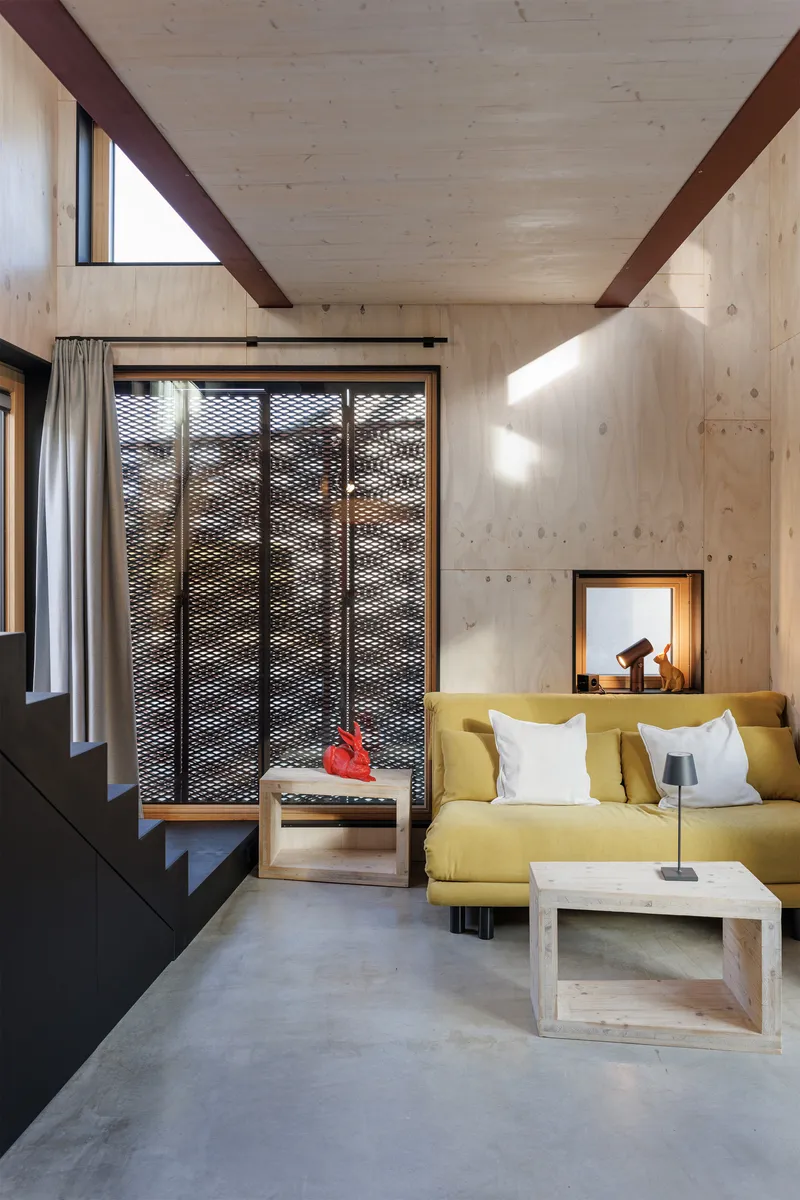 Living room with exposed timber ceiling beams, yellow sofa, and perforated metal screen door panels in natural daylight