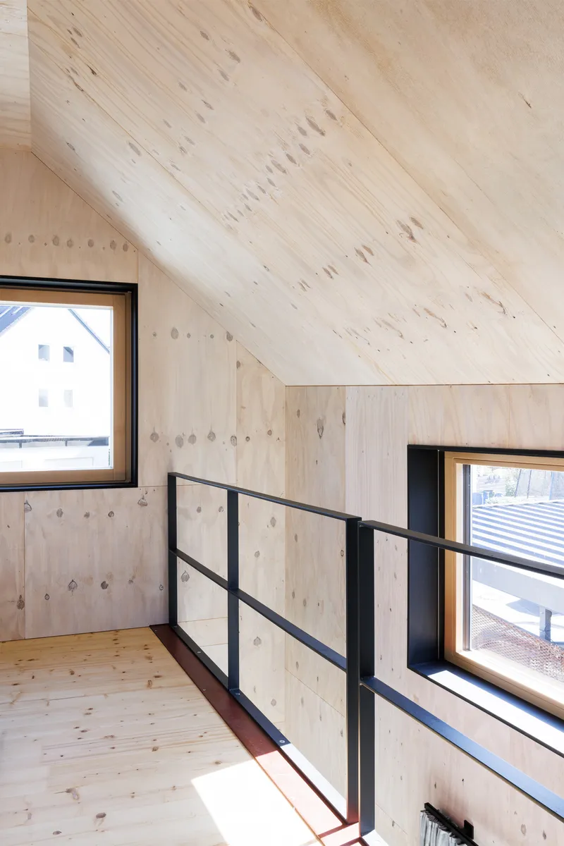 Upper level mezzanine with sloped timber ceiling, black metal railing, and sunlight through framed windows