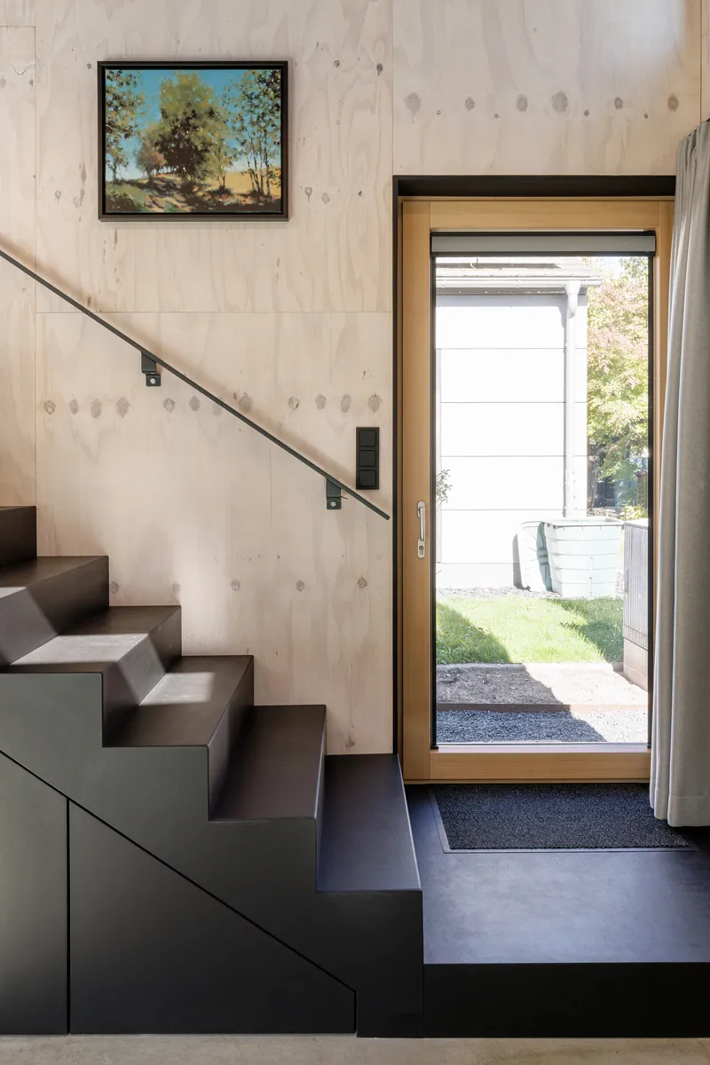 Entry threshold with open timber-framed door revealing garden view beside black metal stair corner