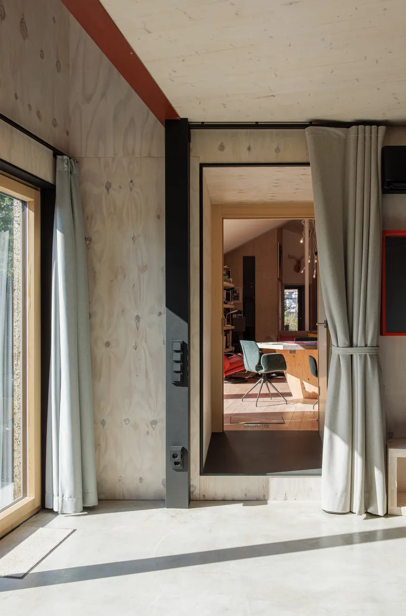 Interior doorway framed in black steel leading from sunlit room through white curtain into workspace beyond