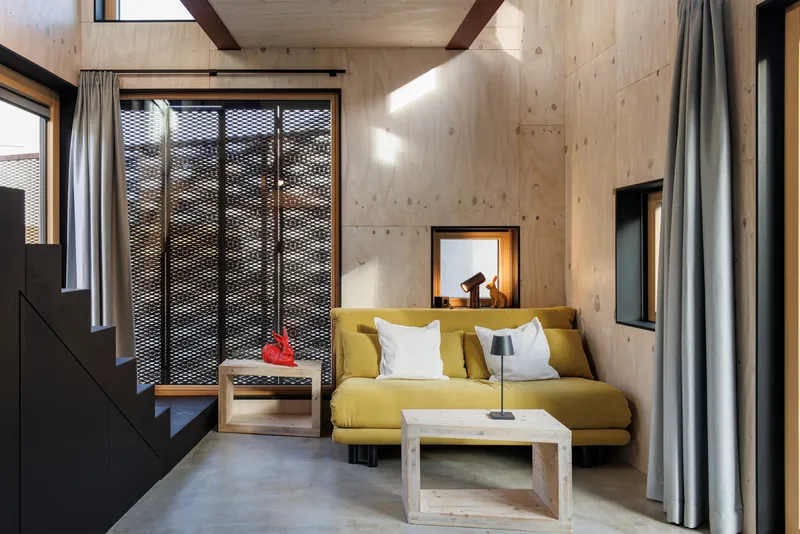 Living room with yellow sofa facing perforated metal sliding doors and light plywood ceiling beams