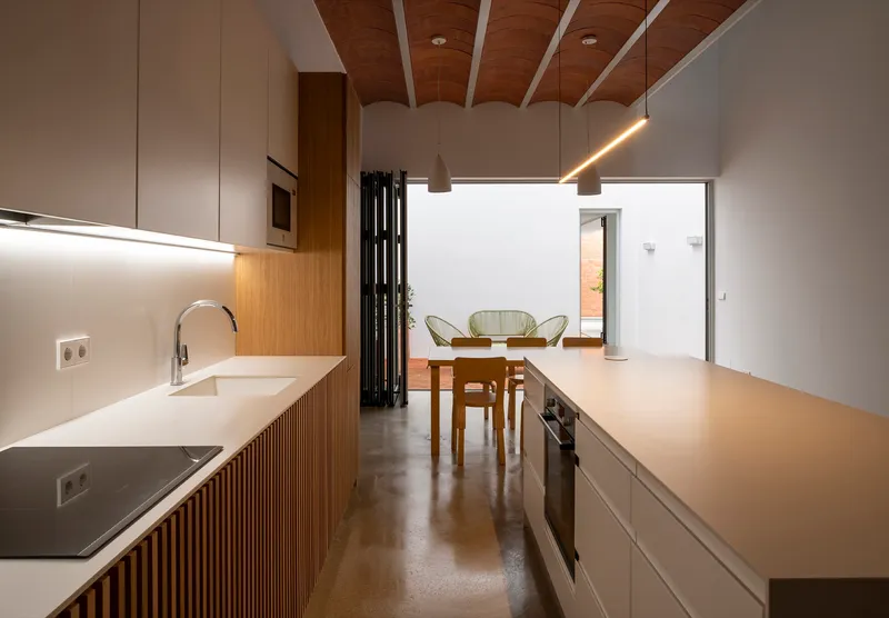Kitchen island with integrated sink and ribbed timber cabinetry beneath a vaulted wood ceiling