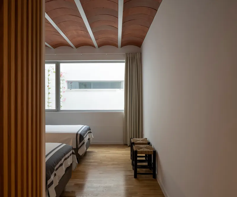 Bedroom with curved timber ceiling beams and horizontal window overlooking neighboring rooftops