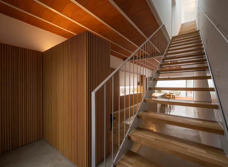 Timber staircase with glass railing and vertical wood slat partition beneath a vaulted ceiling