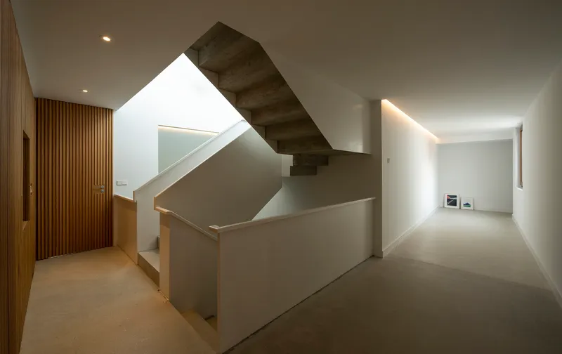 Interior stairwell with cantilevered concrete steps rising through a double-height volume with overhead skylight