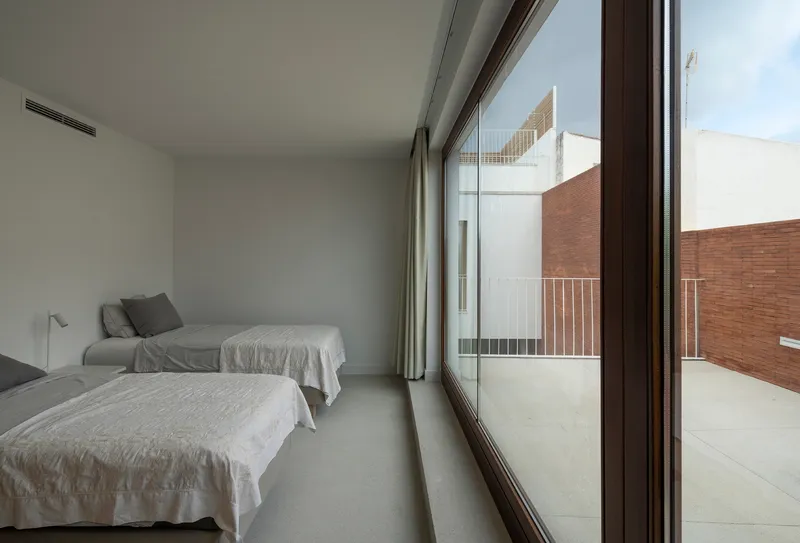 Bedroom with floor-to-ceiling glazing opening onto a private terrace overlooking adjacent brick walls