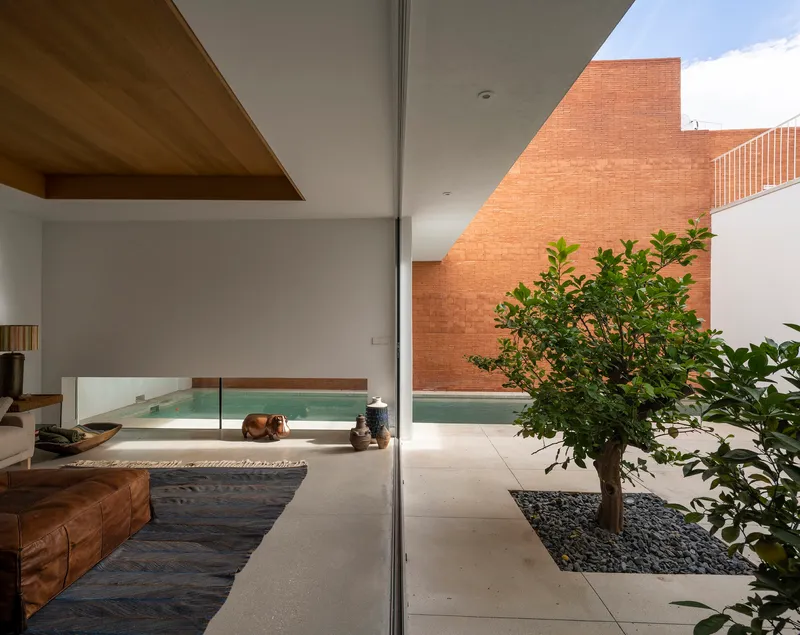 View through floor-to-ceiling glass toward the central courtyard with pool, planted tree and brick wall