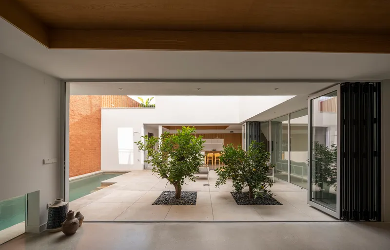 Interior view through folding glass doors to courtyard with two planted trees on concrete pavers
