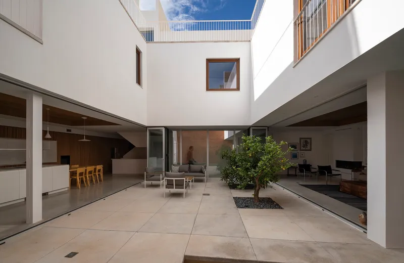 Internal courtyard with a single tree planted in the concrete floor and white walls rising to the sky