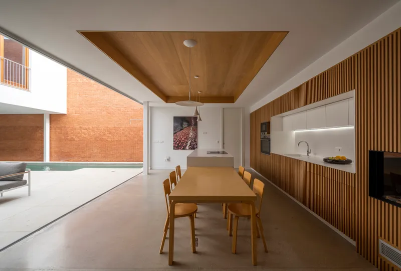 Open-plan dining space with timber ceiling panel and slatted wood kitchen cabinetry overlooking the courtyard