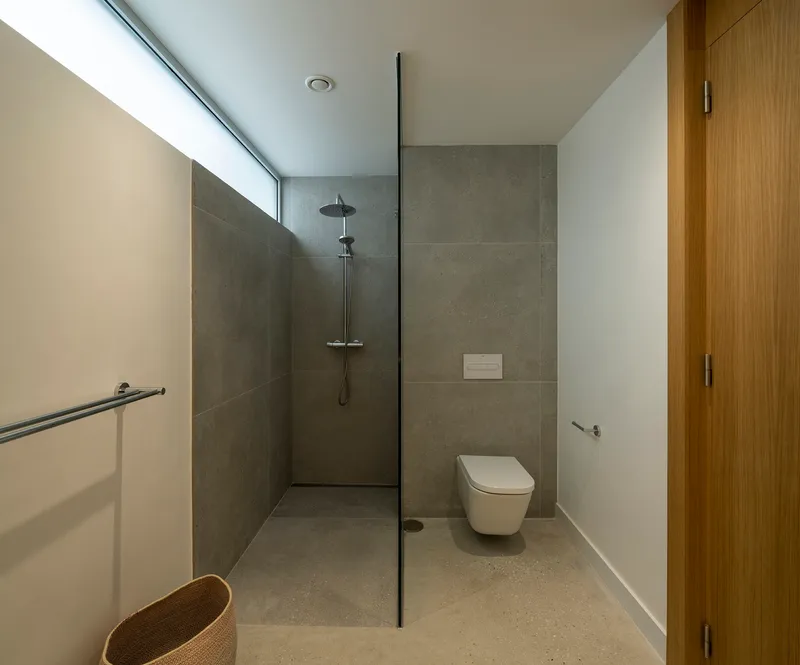 Bathroom with glass-enclosed shower area, grey tile walls and continuous clerestory window above