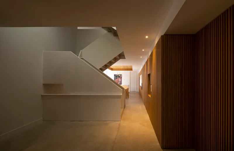 Ground floor hallway with vertical timber slat wall and white plaster staircase under recessed lighting