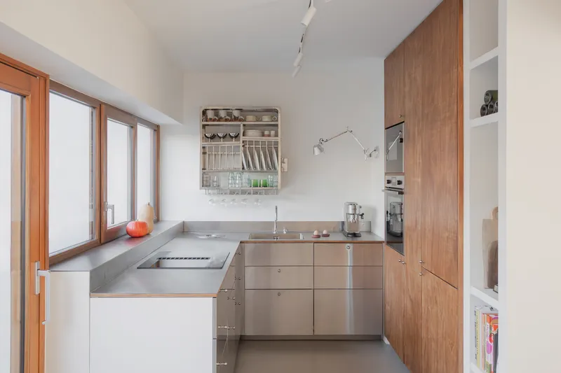 Compact kitchen with stainless steel countertops, timber cabinetry and a tall window overlooking the garden