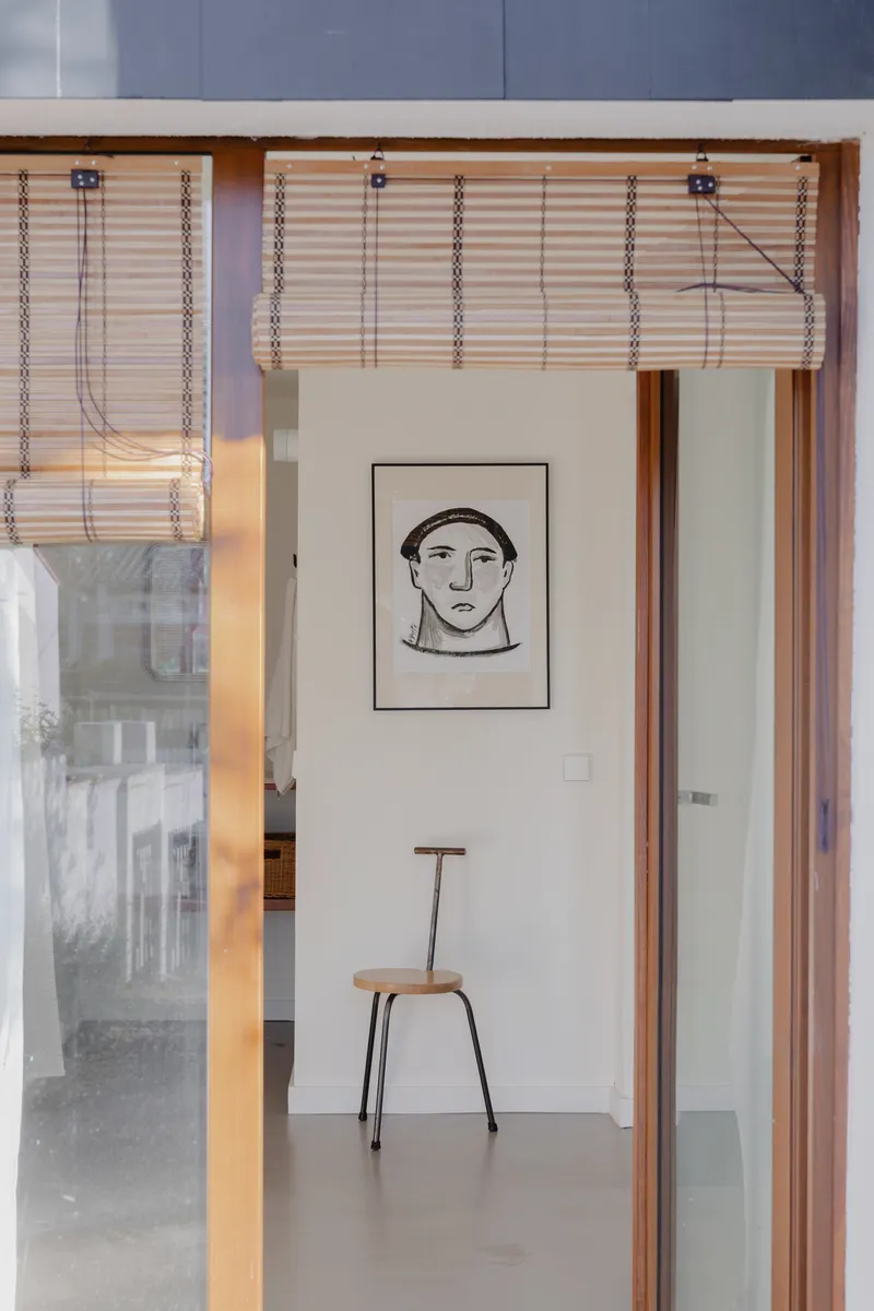 Timber framed doorway with woven bamboo blind leading into a room with a framed portrait and chair