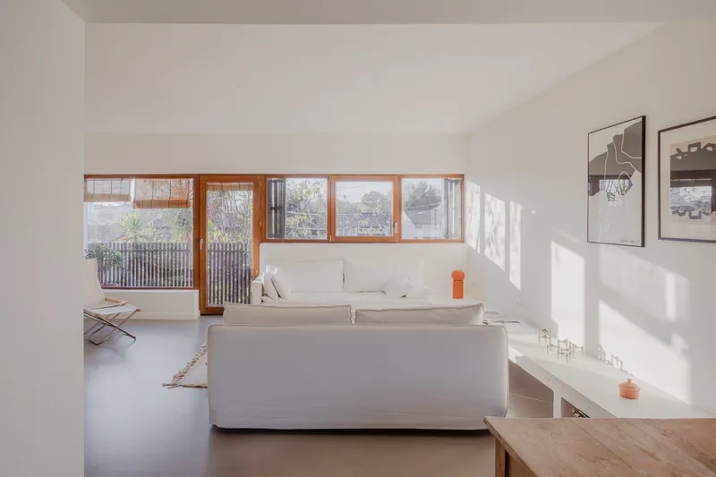 Living room with horizontal timber windows casting sharp shadows on white walls in afternoon light