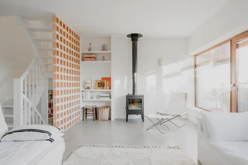 Open plan interior with freestanding black wood stove and timber grid partition beside white painted staircase