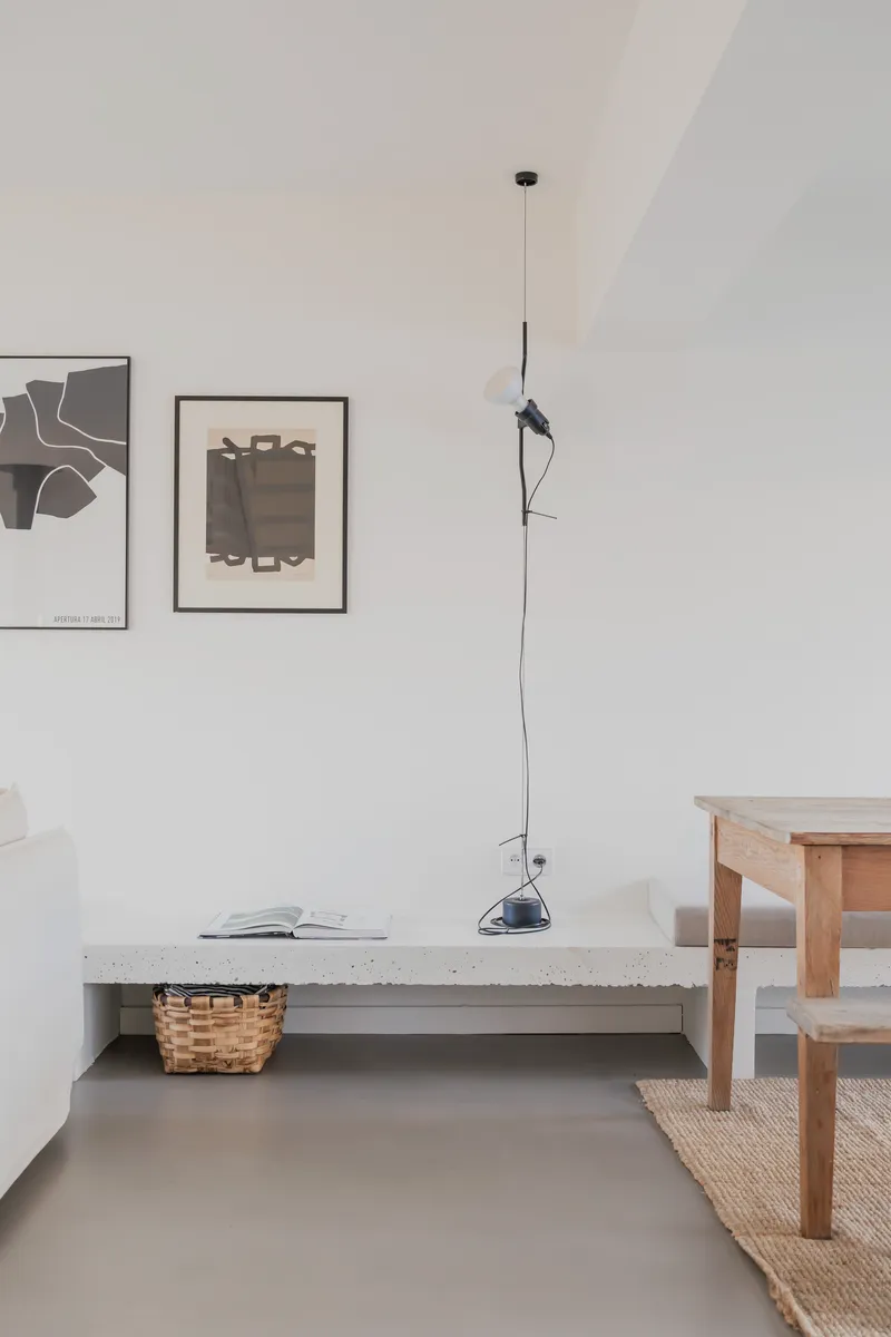 Living area with concrete bench, pendant lamp, framed artworks on white walls and grey polished floor