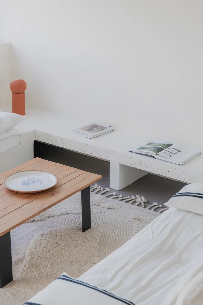 Close-up of concrete bench meeting timber coffee table on woven rug with ceramic plate and magazines