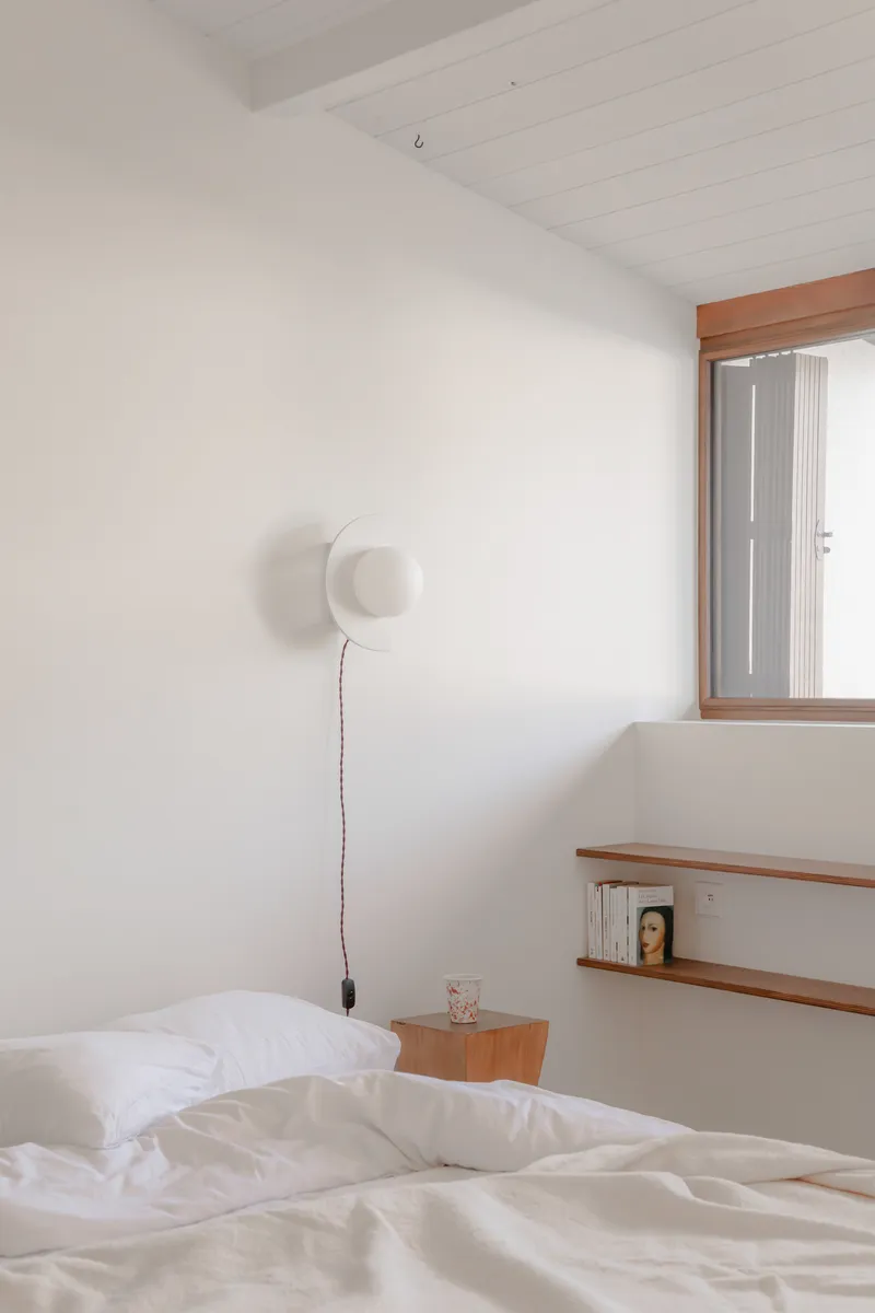 Bedroom corner with timber window frame, wall sconce, open shelving and white painted tongue-and-groove ceiling