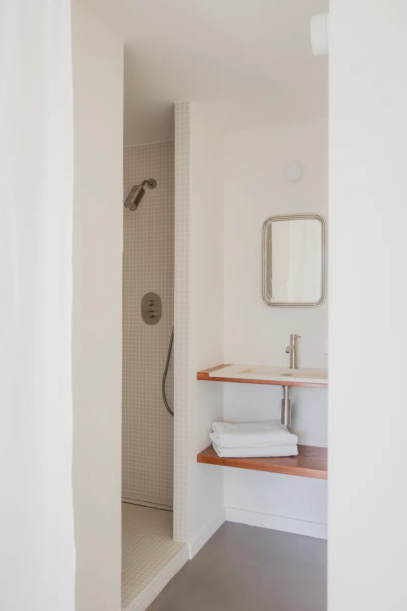 Bathroom view through doorway showing tiled shower niche and floating timber vanity with folded towels