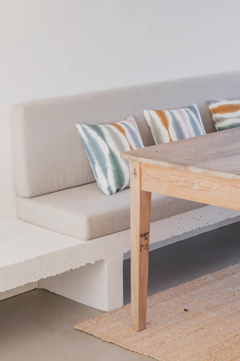 Built-in concrete bench with upholstered seating and striped cushions beneath timber dining table