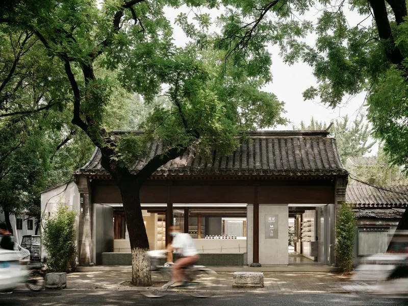 Street view of the pavilion with traditional tiled roof and timber columns framed by mature trees with cyclists passing