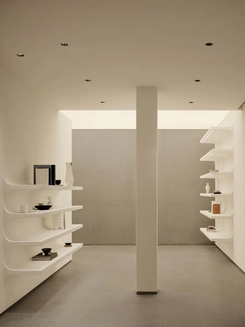 Curved white floating shelves displaying ceramics and books flanking a central column with clerestory windows above