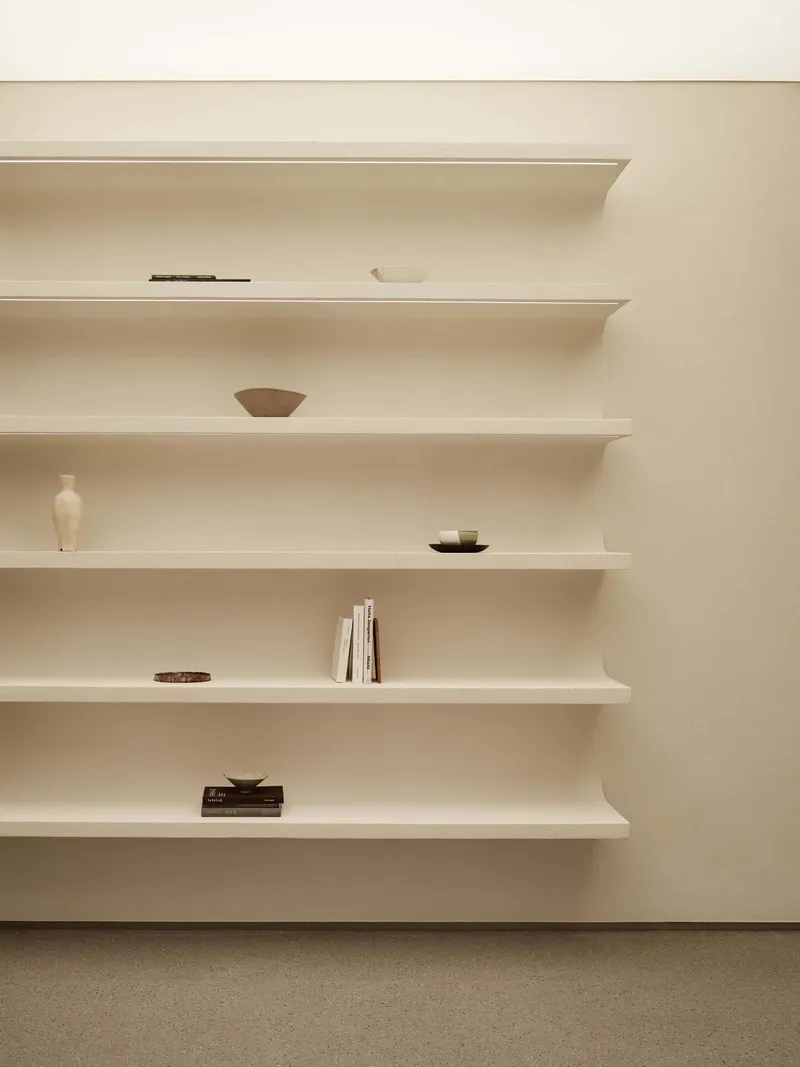 Close-up of rounded white wall-mounted shelves holding sparsely arranged pottery and stacked books