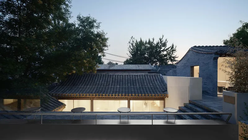 Elevated view of the tiled roof pavilion beside glass-walled volumes and a reflecting pool at dusk